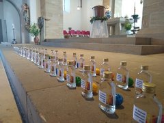 Ein Bild zeigt viele kleine Fläschchen mit Weihwasser aufgereiht in zwei Reihen vor der Altarstufe mit jeweils einem Osterei.